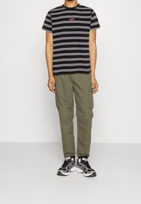 T-shirt à manches courtes rayé noir et blanc avec un logo "Levi's" rouge, associé à un pantalon cargo olive et des baskets noires avec des accents argentés.