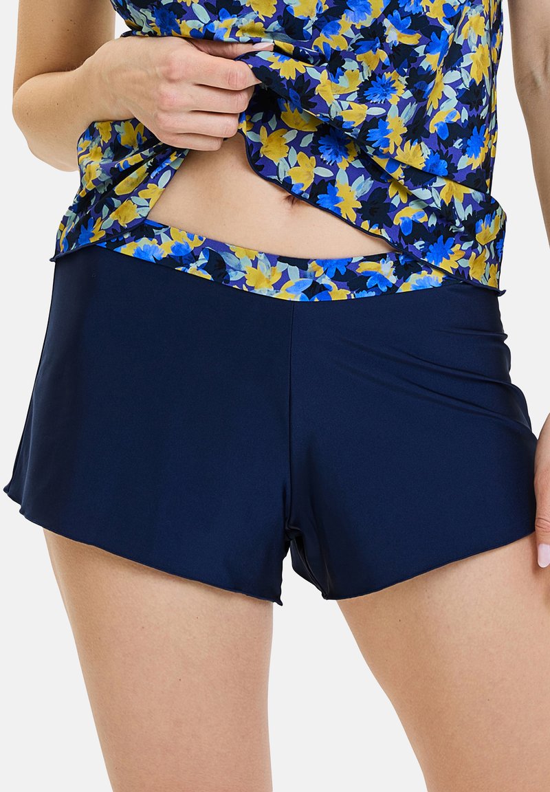 Bañador corto azul marino con diseño acampanado. Cuenta con una cintura con estampado floral en amarillo y azul. Fabricado con tejido suave y elástico.