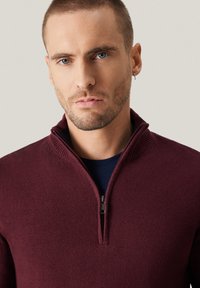 Bordowy sweter z zamkiem i stójką oraz fakturowanym splotem. Pod spodem warstwowa granatowa koszula. Proste, funkcjonalne zapięcie na zamek.