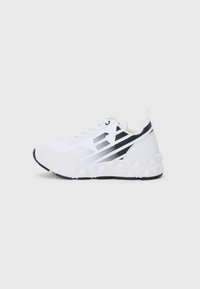Baskets de sport blanches avec des accents noirs, présentant une semelle intermédiaire texturée et des motifs géométriques. Des lacets et une boucle au talon sont présents.