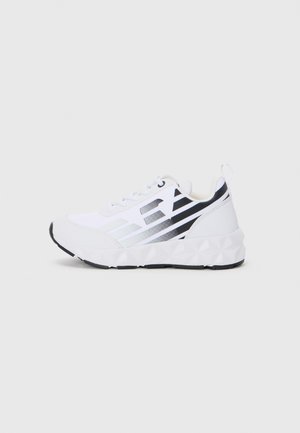 Baskets de sport blanches avec des accents noirs, présentant une semelle intermédiaire texturée et des motifs géométriques. Des lacets et une boucle au talon sont présents.
