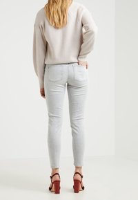 Jasnoszare skinny jeans z wysokim stanem i tylnymi kieszeniami, zestawione z luźnym, prążkowanym beżowym swetrem oraz czerwonymi sandałami na słupku.