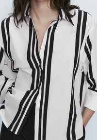 Chemise boutonnée à rayures noir et blanc avec un col, manches longues retroussées et un tissu léger au toucher doux.