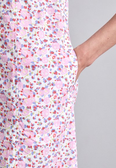 Cvečni plašč z belim ozadjem, okrašenim z roza, rdečimi in modrimi vzorci. Vidna je žep, plašč pa ima gladko bombažno teksturo.