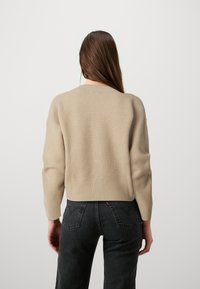 Beige ribbstickad tröja med långa ärmar och rund halsringning, med en kortare passform och texturerad yta. Bärs tillsammans med mörka jeans.
