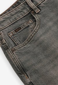Jeans din denim gri, cu un design standard cu cinci buzunare, cusături în contrast și un mic etichetă din țesătură pe buzunarul din spate.