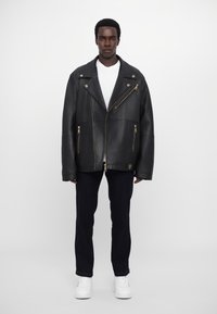 Μαύρο δερμάτινο μπουφάν μοτοσικλέτας με oversized εφαρμογή, ασυμμετρικό κλείσιμο φερμουάρ και χρυσά αξεσουάρ. Φορώντας πάνω από λευκό T-shirt και σκούρα τζιν.