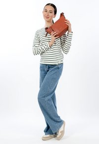 Sarkans ādas plecu somiņa ar rāvējslēdzēja aizdari, noņemamu siksnu un salokāmu dizainu. Modelis valkā svītrainu kreklu un augsta vidukļa džinsus.