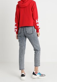 Felpa rossa corta con testo stampato bianco sulle maniche, abbinata a jeans grigi chiari a vita alta con una finitura testurizzata e orlo sfilacciato.