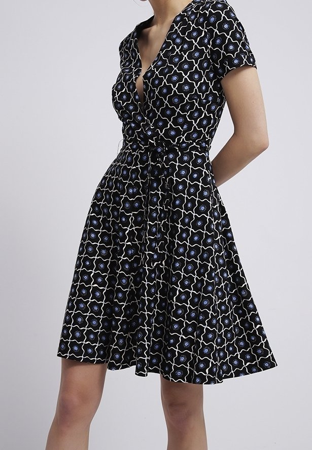 Svart omlottklänning med v-ringning, korta ärmar, åtsittande midja och cirkulärt blått blommönster på vit bakgrund. Luftig kjol.