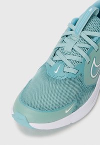 Scarpa sportiva azzurra chiara con tomaia in rete, dettagli testurizzati, logo Nike bianco e linguetta imbottita. Suola liscia con bordo bianco a contrasto.
