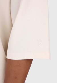 Beige bomulds t-shirtærme med et subtilt præg af "B" logo. Har en glat tekstur og en pænt syet søm.