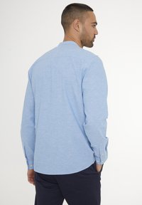 Camisa de manga larga de color azul claro con puños de botón, cuello y tejido texturizado. Estilizada con un dobladillo curvado y detalle en el yugo trasero.