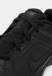 Mustaline mustrees, millel on tekstureeritud sünteetiline ülemine pool, paeltesüsteem, pehmendatud krae ja peene brändingu detail küljes samas toonis.