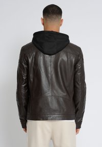 Brun læderjakke med sort hætte, udstyret med quiltede skulderdetaljer og en skræddersyet pasform. Glat tekstur og minimalistisk design.