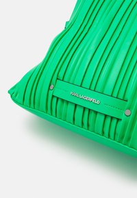 Vihreä, laskostettu keinonahkainen käsilaukku kiiltävällä pinnalla. Varustettu hopeisilla yksityiskohdilla ja merkkilapulla, jossa on kohokuvioitu "KARL LAGERFELD".