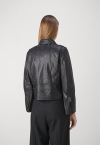 Sort læder cropped jakke med krave, synlig syning og lynlåsærmer. Teksturfinish, tætsiddende design og knapdetaljer.