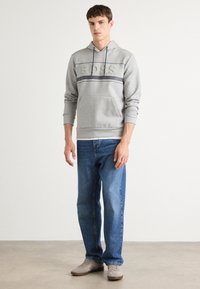 Gray hoodie with a textured "BOSS" logo, featuring a striped design and a kangaroo pocket, paired with blue jeans and light gray sneakers.