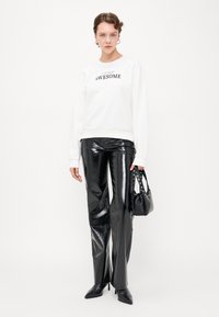 Weißer Sweatshirt mit dem Text "AWESOME", kombiniert mit glänzenden schwarzen Pseudo-Leder-Hosen und einer kleinen schwarzen Handtasche mit Nietengriffen.