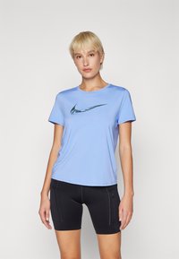 Camiseta deportiva azul claro hecha de tela suave, con un logo de Nike en verde oscuro. Combinada con pantalones cortos negros que presentan un diseño ajustado.
