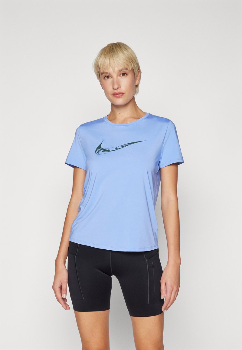 Camiseta deportiva azul claro hecha de tela suave, con un logo de Nike en verde oscuro. Combinada con pantalones cortos negros que presentan un diseño ajustado.