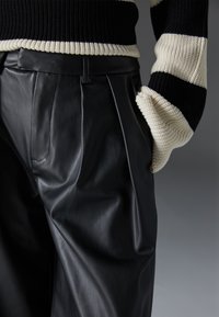 Black leather trousers with a smooth texture and pleated design, paired with a striped knitted sweater featuring black and cream colors.