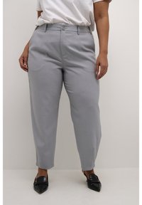 Pantalones tailor grises claros con pierna recta, cierre de botón, lazos para cinturón y aberturas laterales, combinados con mocasines negros.