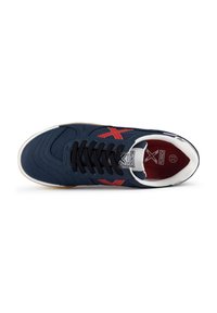 Zapatilla de deporte de color azul oscuro con cordones negros, diseño de acentos rojos y suela blanca. Presenta un cuello acolchado y parte superior de tela texturizada.