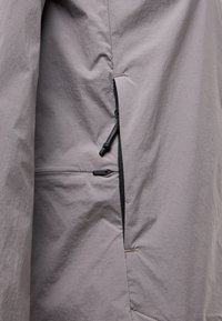 Light gray fabric jacket featuring a textured surface, side zip pocket with black zipper pull, and minimalist design with clean seams.