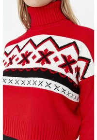 Rode gebreide coltrui met een geometrisch patroon in wit, zwart en rood op de schouders. De textuur is glad met geribde boorden en zoom.