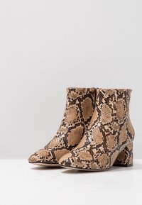 Botines de punta afilada en un patrón de serpiente en tonos marrón y beige, con un upper texturizado y un tacón robusto para mayor estabilidad.