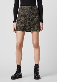 Falda de estampado de leopardo en tejido verde oliva con una cremallera plateada en el centro. Combinada con botas de tobillo negras con cordones para crear contraste.