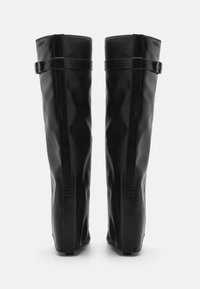 Botas negras de cuero por encima de la rodilla con una textura suave, que cuentan con un diseño minimalista y una hebilla lateral para el ajuste.