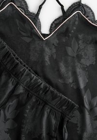 Musta satiinisatiini toppi, jossa on kukkakuosi ja pitsireunus. Elastinen vyötärö matching shortsit, joissa on gathered-yksityiskohtia. Korostava kontrastivärinen ommel.