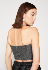 Čierny crop top bez ramienok s trblietavým povrchom a zipsom vzadu. Vytvorené s čiernymi nohavicami a strieborným reťazovým náhrdelníkom.