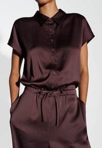 Chemise bourgogne à manches courtes avec un devant boutonné, en tissu texturé, et une taille nouée, présentant une coupe décontractée et un col.