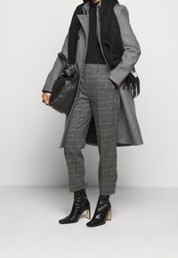 Manteau en laine gris, col roulé noir, pantalon à carreaux gris, sac en cuir noir et bottines noires à talons avec une finition texturée.