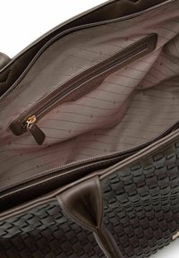 Bolso tote tejido marrón con asas de cuero suave. El interior cuenta con un bolsillo con cremallera y un forro suave con estampado en tonos beige.