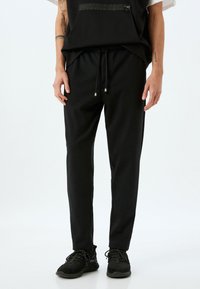 Pantalones de chándal negros hechos de tejido suave; con cintura elástica con cordón, ajuste ajustado y bolsillos laterales.