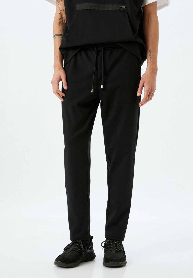 Pantalones de chándal negros hechos de tejido suave; con cintura elástica con cordón, ajuste ajustado y bolsillos laterales.