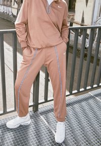 Tan Nike zip-up tröja med rutigt krage, i kombination med matchande tan-byxor med vita sidoställningar, bärs med vita sneakers.