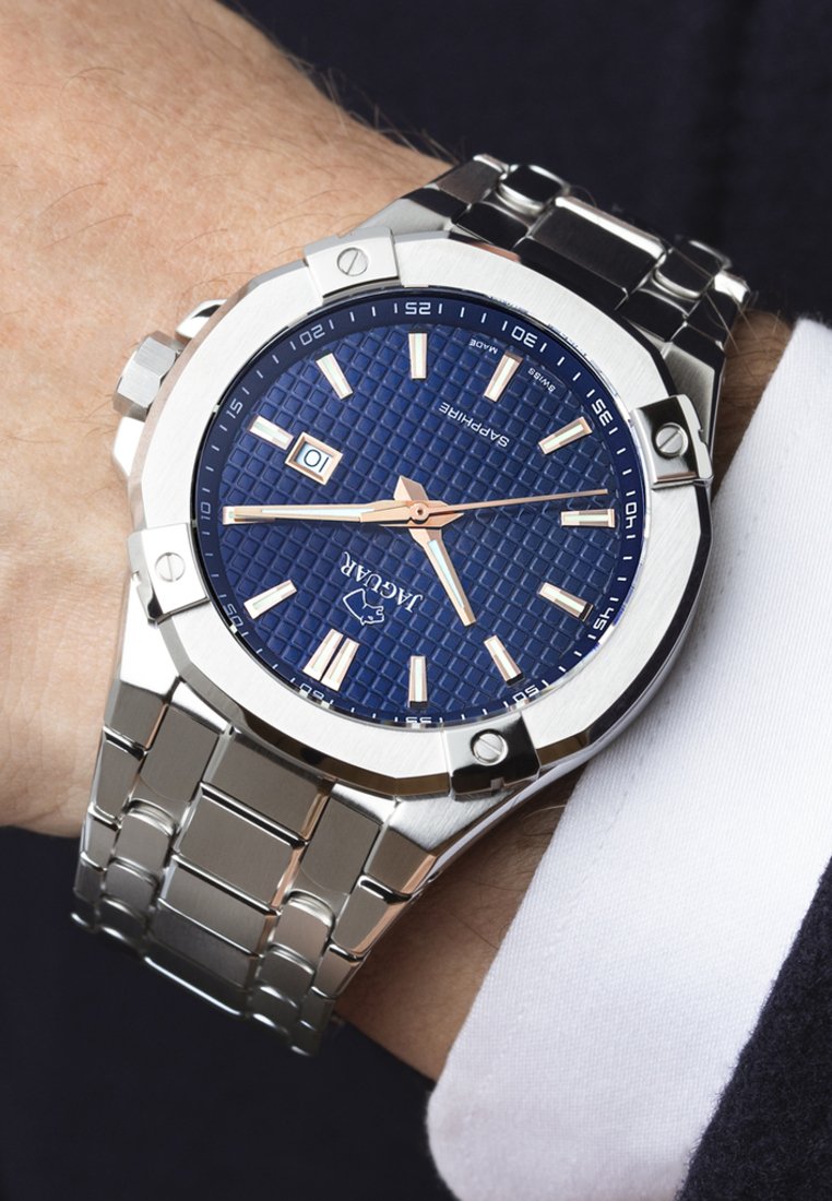 Reloj de pulsera de acero inoxidable con una esfera azul texturizada, acentos en oro rosa y una brazalete de eslabones plateados. Presenta una ventana de fecha a las 3 en punto.