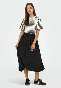 Randig kortärmad t-shirt i krämfärgad och svart, tillsammans med en svart, flödande, ankellång kjol med resår i midjan och sidfickor.