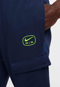 Granatowe dresy o fakturowanej powierzchni, z zielonym logo Nike AIR oraz boczną kieszenią. Zawierają niebieskie akcenty przy szwie.