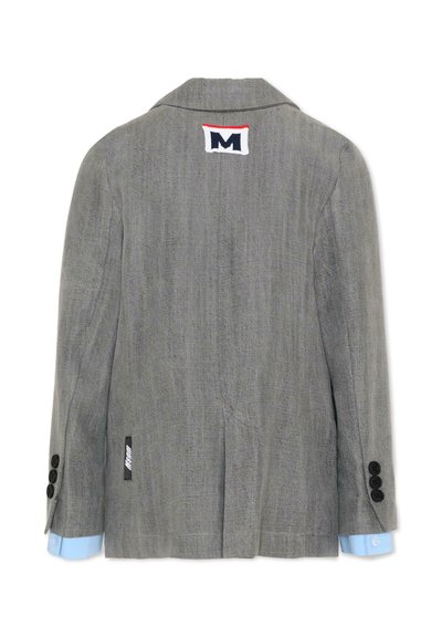 Blazer texturizado gris con puños de camisa azul claro, botones negros en las mangas y parche blanco con una "M" azul marino y una línea roja en la parte trasera del cuello.