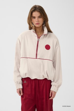 Young woman wearing a white half-zip jacket with red trim and logo, paired with red drawstring pants against a plain light background.