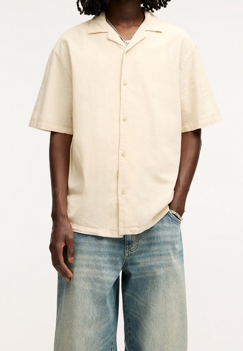 Kortärmad, knapp-up skjorta i ljusbeige tyg, med en camp collar, avslappnad passform och en jämn yta. Kombinerad med urtvättade blå jeans.