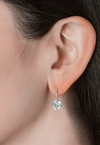 Orecchini in argento con una pietra preziosa trasparente a forma di diamante sospesa da un delicato gancio. Il design presenta una leggera texture sul metallo.