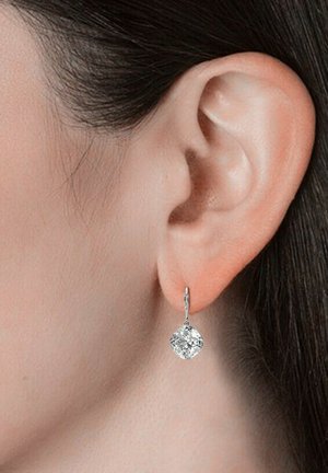 Orecchini in argento con una pietra preziosa trasparente a forma di diamante sospesa da un delicato gancio. Il design presenta una leggera texture sul metallo.