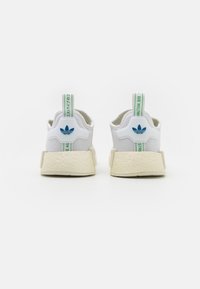 Zapatillas blancas con parte superior de malla, detalles en verde y azul, suela gruesa y texturizada, y logotipo distintivo en la parte posterior. Lengüetas reforzadas.